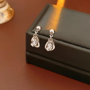 Macro shot of sparkling teardrop zircon earrings on a textured dark jewelry box
