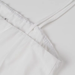 Detail of white cotton pleated dress featuring thin spaghetti straps and small 'C' label