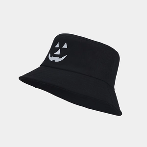 Detail view of a black Halloween bucket hat with a white pumpkin face print on a grey background