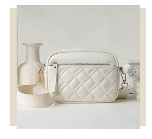 Detail of white quilted crossbody bag with wide strap and gold-tone metal zipper