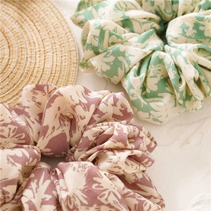 Detailed view of floral oversized fabric scrunchies in green and purple on a rustic mat