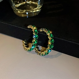 Close-up of golden C-shaped hoop earrings with emerald green zircon stones on black background