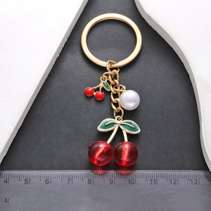 Golden cherry keychain with red resin pendant and white pearl on black background
