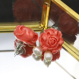 Elegant coral pink floral earrings with white pearls on a reflective mirror background