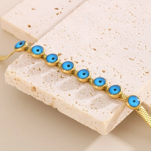 Macro shot of gold snake chain bracelet featuring blue evil eye charms on stone