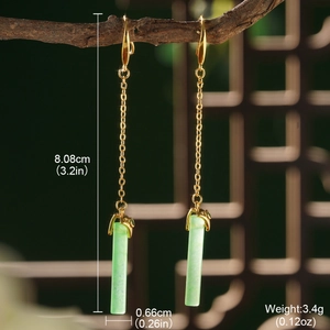 Detail shot of long gold earrings with green jade-like pendants on wooden background