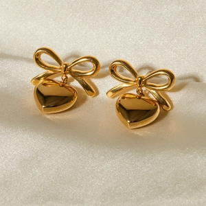 Macro detail of gold bow and heart earrings on silk texture with high polish finish