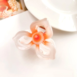 Macro view of floral hair claw clip featuring orange-white gradient petals and golden spring