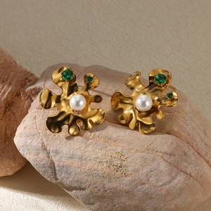 Macro detail of gold flower earrings with white pearl and green stone on rock
