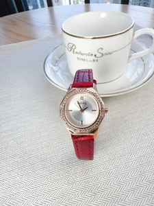 Detail of red leather strap watch with rose gold diamond bezel on a white textured surface