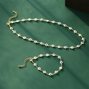 Gold evil eye jewelry set with blue enamel beads necklace and bracelet on green background