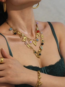 Detailed view of layered 18k gold necklaces and colorful stone heart pendants on a model