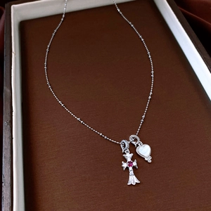 Detailed close-up of a silver cross pendant with red gem and mother of pearl heart necklace