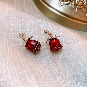 Elegant red rose stud earrings with gold metal base on a white textured background