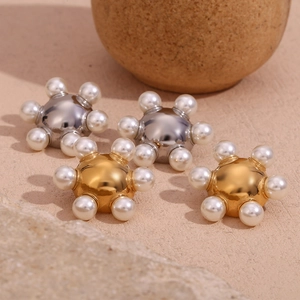 Close-up of starburst pearl earrings in gold and silver finish on textured pedestal