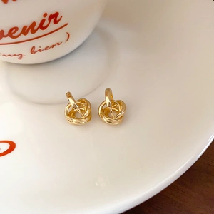 Close-up of golden twist knot earrings displayed on a white plate in a French style