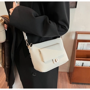 Detail shot of a white corduroy shoulder bag showing vertical texture and gold metal twist lock