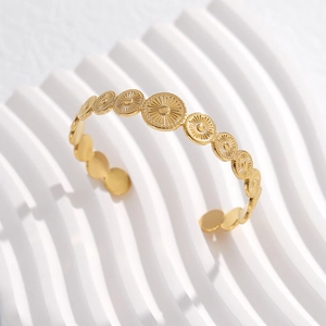 Macro detail of gold-tone cuff bracelet with sunburst texture on a wavy background
