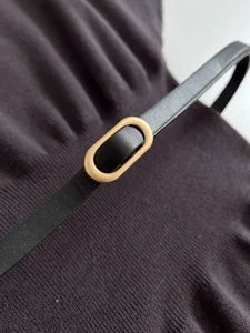 Detail of slim black leather belt featuring a modern oval gold metal buckle and texture