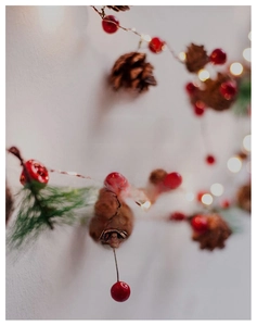 Close-up of Christmas string lights with red berries, pinecones and warm glowing LEDs