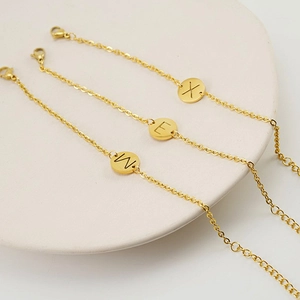Detailed view of three gold-plated titanium steel chain bracelets with letter charms X, E, M