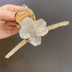 Detail of a golden metal hair claw clip featuring a large pearlescent white 3D floral design