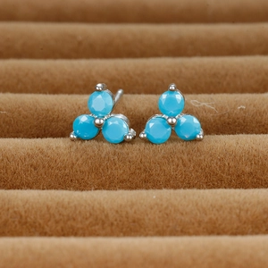 Macro shot of silver clover stud earrings featuring round turquoise stones on velvet tray