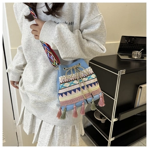 Detail of light blue bucket bag featuring colorful ethnic embroidery and fringe accents