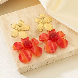 Elegant gold metal and red resin double flower earrings on a marble display block