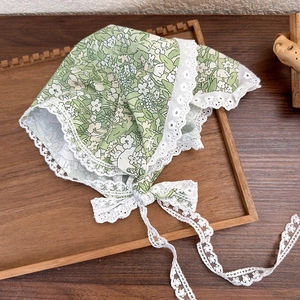 Detailed view of green floral baby bonnet with intricate white lace trim on wooden tray