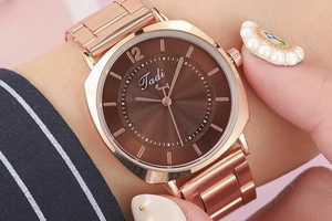 Detailed close-up of rose gold steel watch featuring a sunburst brown dial on a wrist