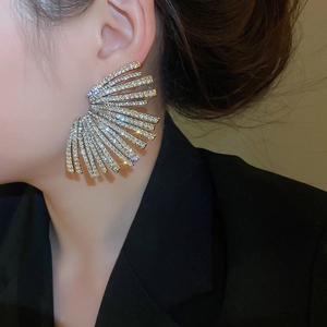Macro shot of oversized fan-shaped stud earrings with sparkling pavé crystals on a model