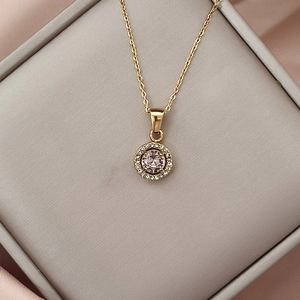Close-up of golden necklace featuring a pink zircon pendant surrounded by white crystals