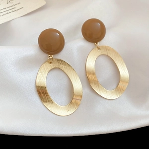 Close-up of golden brushed oval metal earrings with caramel resin studs on white silk