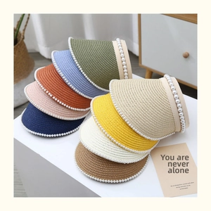 Detail view of woven straw sun visors with pearl accents in nine vibrant colors on a table