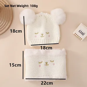 Detailed view of white knitted baby set including earflap hat with faux fur pom poms