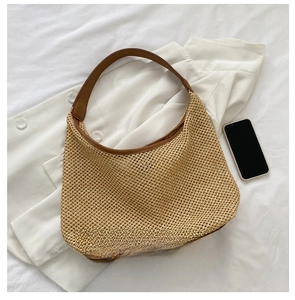 Straw shoulder bag with brown leather handles showing interior capacity next to phone