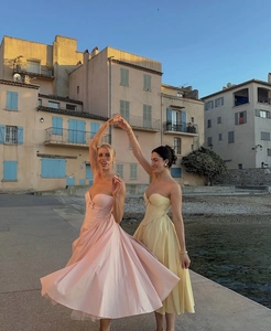 Detail of pink and yellow strapless corseted maxi dresses with bow accents and flared skirts