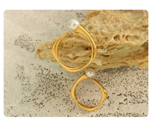 Macro shot of gold-plated C-shaped earrings with pearls on a textured stone surface