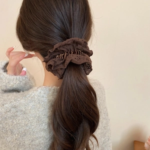 Detail of dark brown lace scrunchie worn on a ponytail against a neutral wall