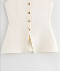 Détail d'un haut en maille blanc cassé avec quatre boutons dorés et une fente centrale