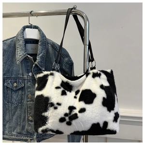 Detail showing plush cow print tote bag with black strap hanging on a metal rack