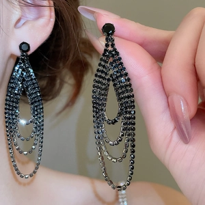 Détail de boucles d'oreilles à pompons en strass noirs multicouches portées par un modèle