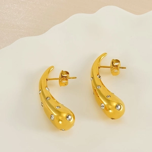 Macro shot of gold teardrop earrings with shimmering crystal accents on wavy background