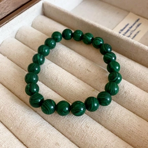 Close-up of green malachite beaded bracelet resting on beige velvet jewelry box tray