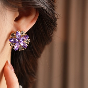 Dettaglio di orecchini a fiore viola con strass indossati su un orecchio