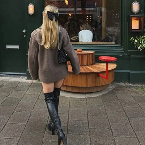 Street style view of a brown wool coat with black high boots and a bow hair accessory
