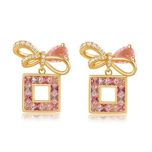 Detailed shot of gold bow stud earrings with pink gemstone and square crystal pendants