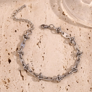 Close-up of silver knot and coffee bean link chain with lobster clasp on stone surface