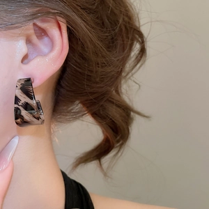 Close-up of a large leopard print acrylic C-shaped earring worn on a model's ear